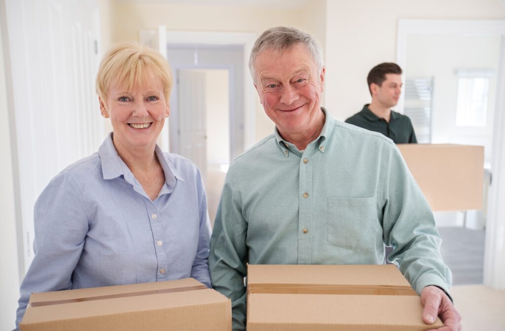 A senior couple holding moving boxes, preparing to downsize by moving into a senior living community