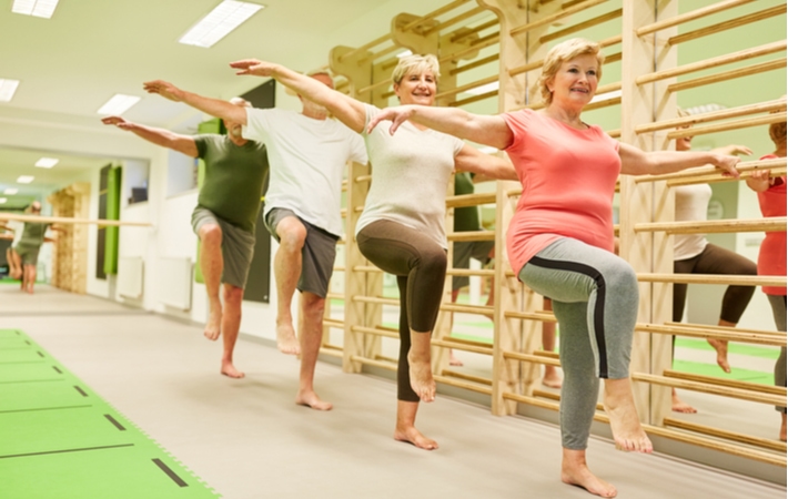 A group of four seniors in an exercise class, standing on one foot to strengthen their balance