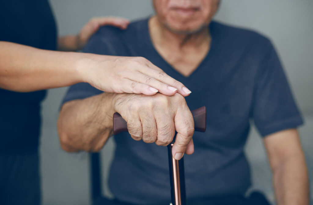 a man sits and holds a cane, while someone from out of frame places their hand over his in support