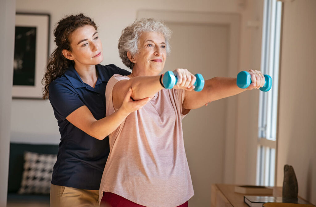 A physiotherapist assisting her patient to lift dumbells.