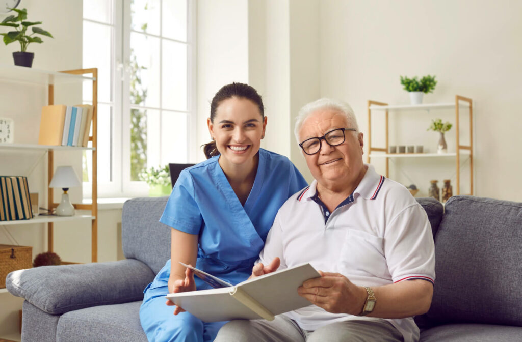 A senior man and his caregiver looking through a photo album and smiling at the camera in memory care.