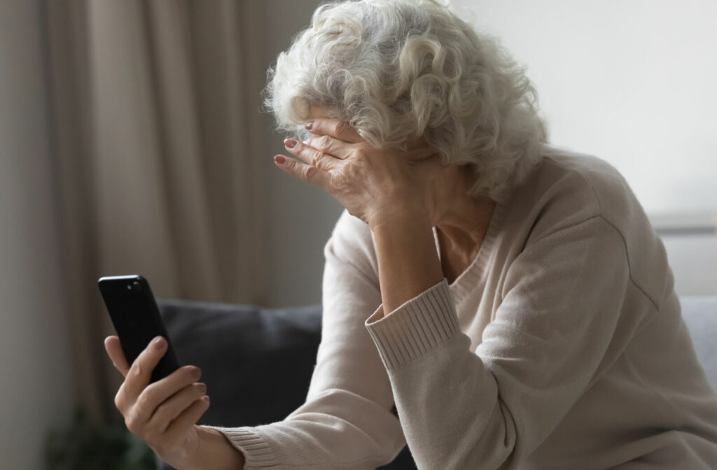 An older adult with dementia raising a hand to their forehead in frustration at their phone.