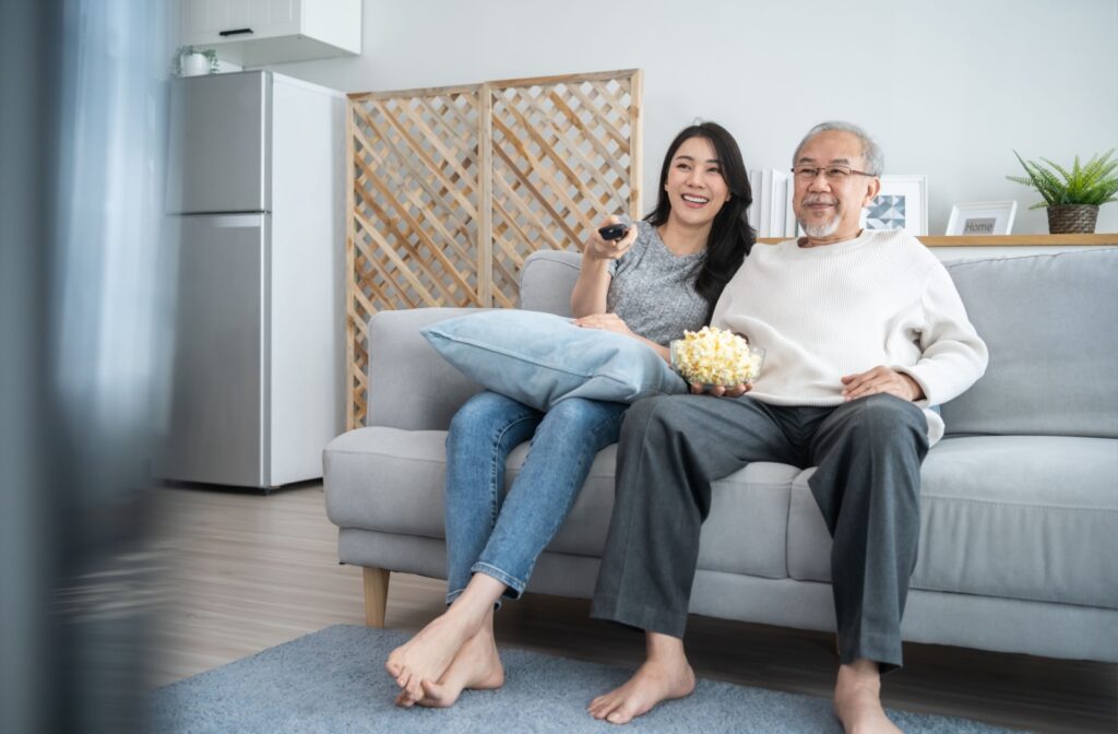 An adult child and their older parent sitting on a couch watching a movie together.