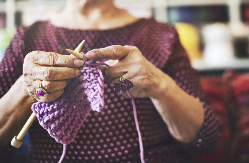 A senior wearing a purple shirt and purple rings, begins knitting a project with a purple yarn