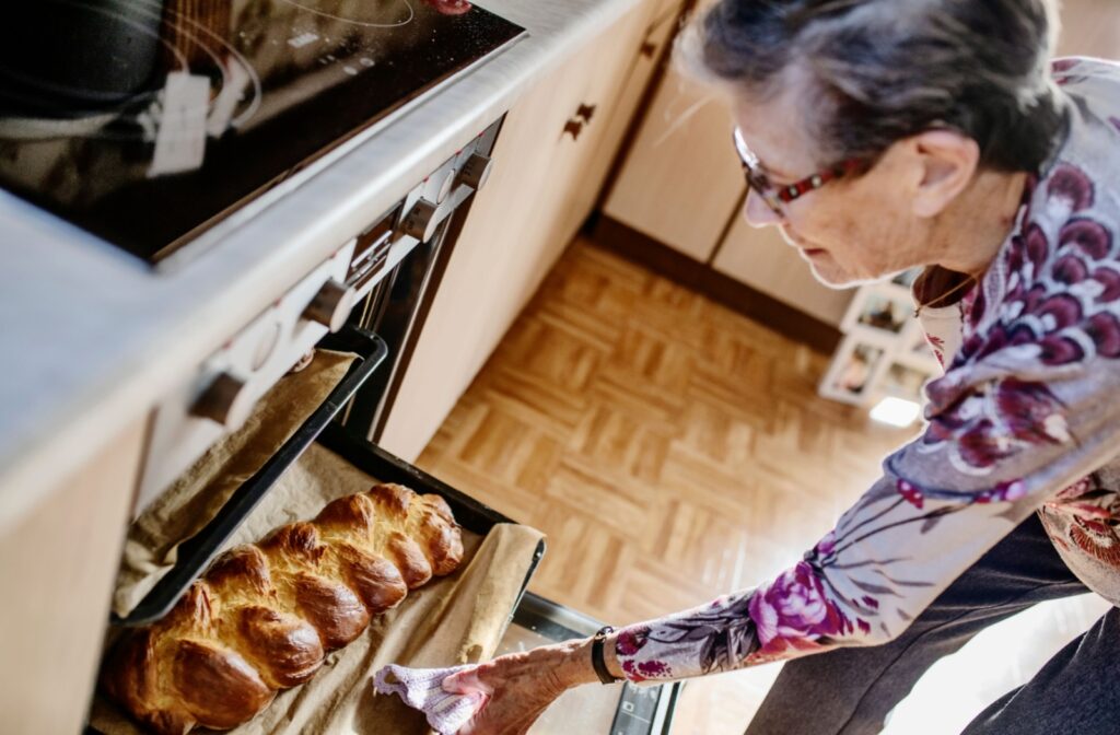 An older adult pulls some freshly baked bread from her oven in the kitchen.